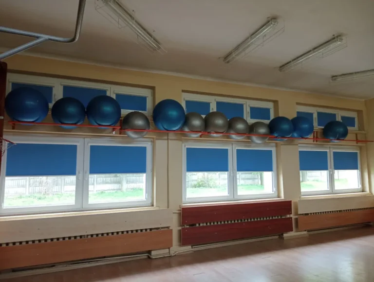 Niebieskie rolety materiałowe z prowadnicą na sali gimnastycznej- Agmart producent rolet