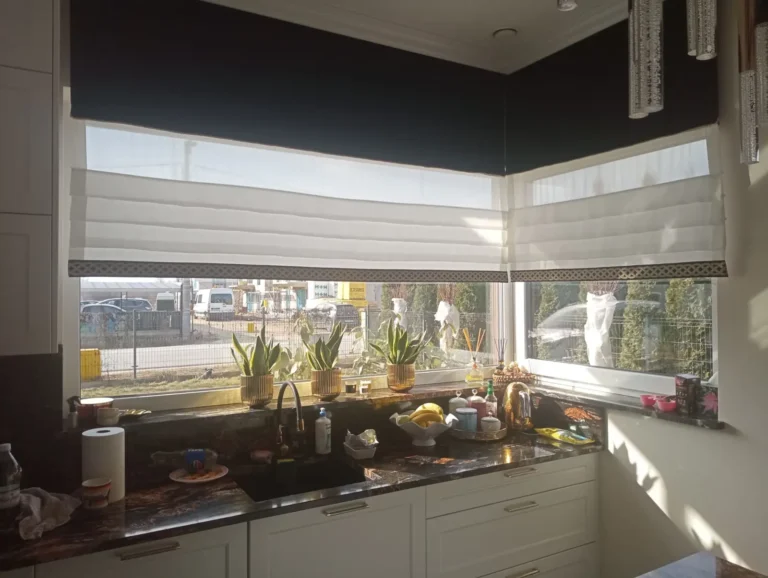 Biała roleta rzymska z ciemnym wykończeniem w oknie kuchennym